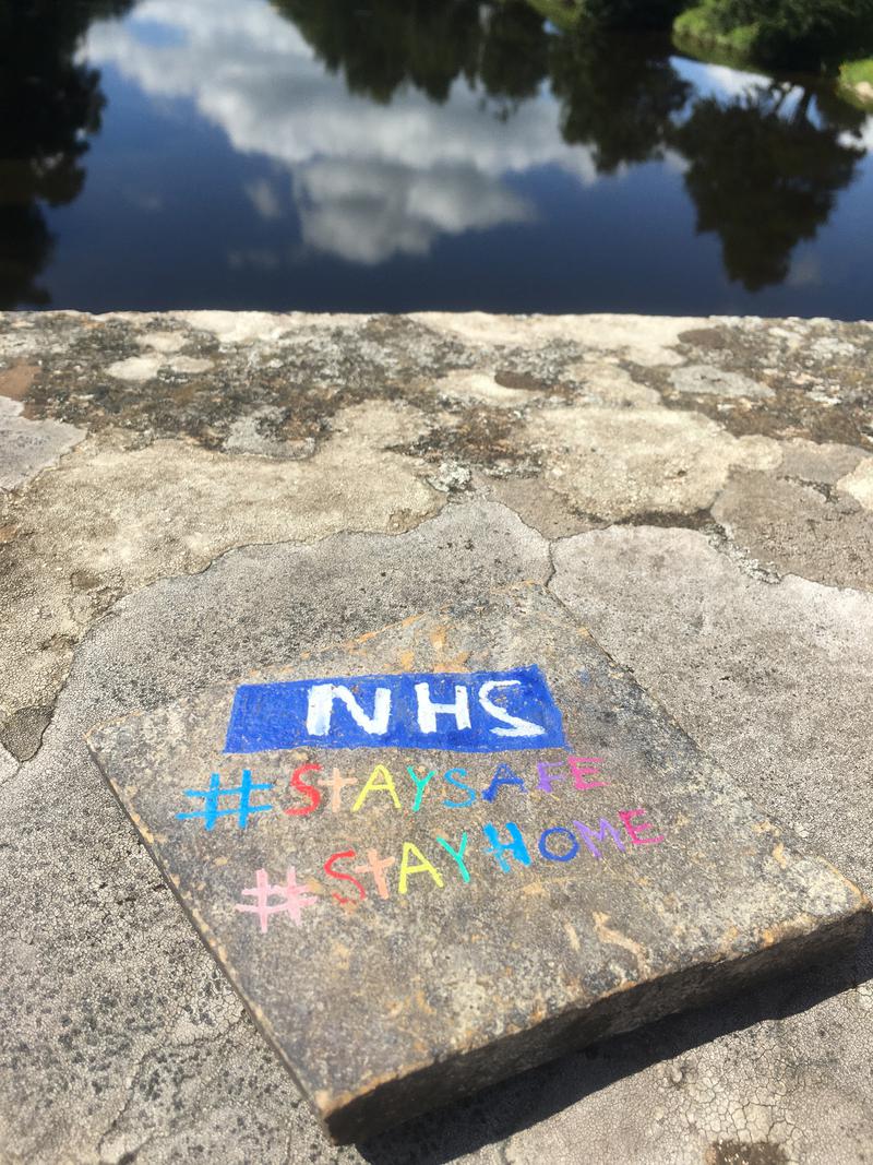 A pebble painted with the NHS logo and #Staysafe #Stayhome. On Boughrood Bridge, over the River Wye, Boughrood, Powys.