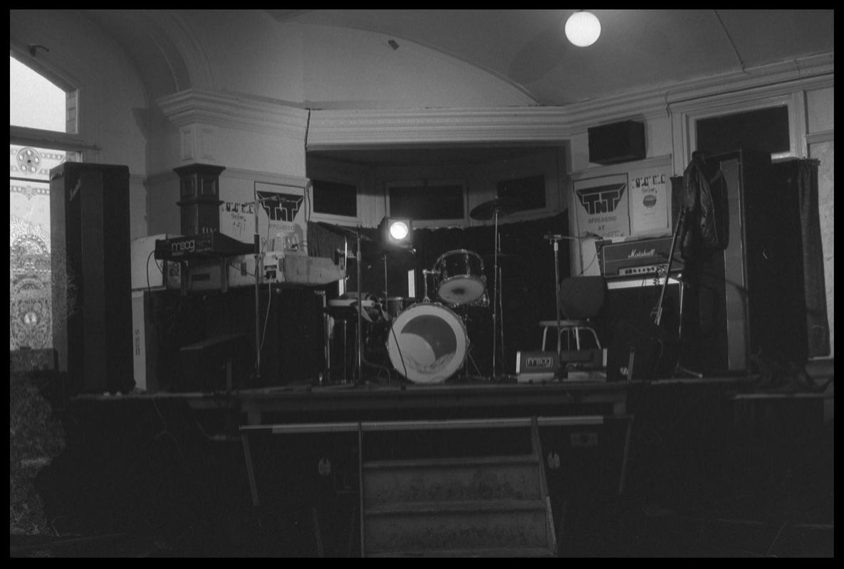 TNT Group&#039;s musical instruments on stage in corner of room. Location unknown.