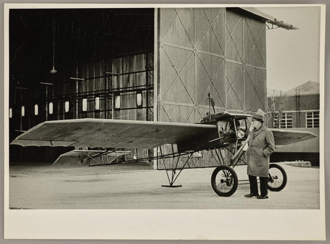 View of C.H. Watkins standing next to the Robin Goch infront of a hangar.