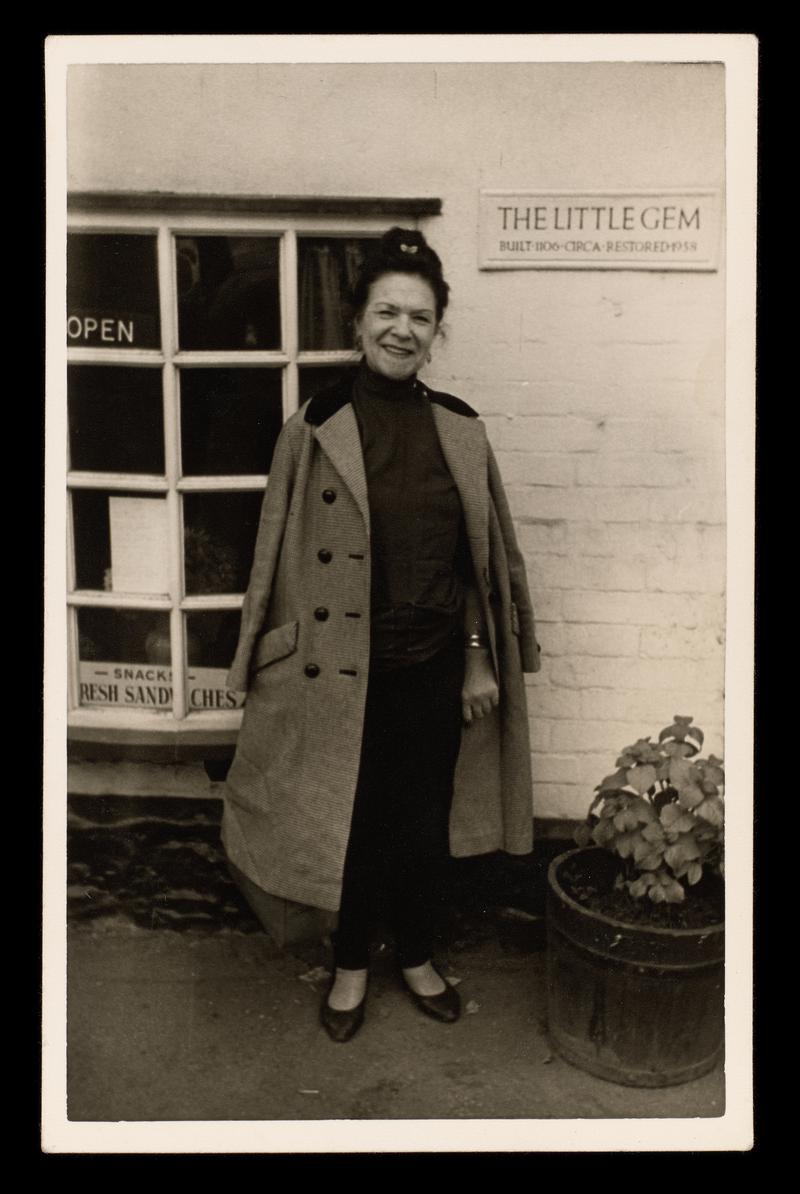 Black and white photograph of female ( possibly Jessie Knight) standing outside a shop.