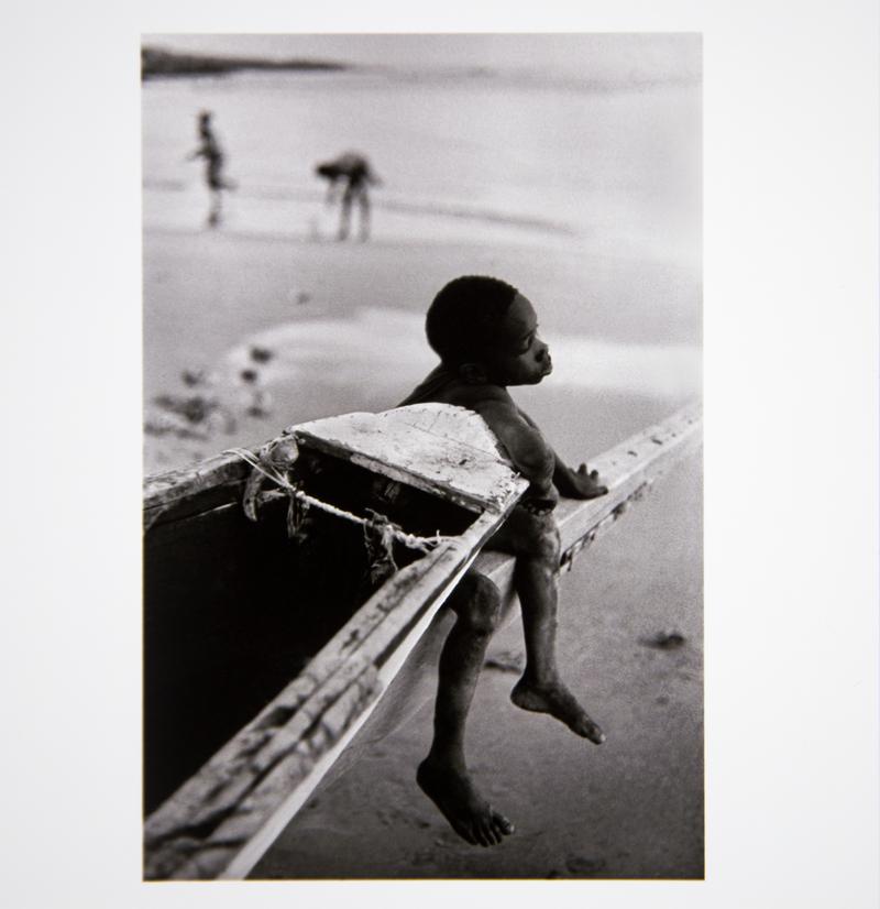Small boy dreams whilst sitting on the prow of a fishing boat drawn onto the beach. Dakar, Senegal