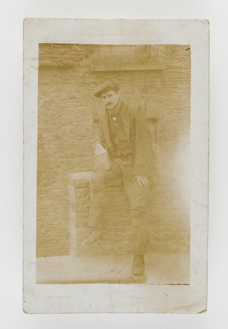 Photograph of a miner sitting on a wall holding a bottle.  Taken at Ty&#039;n y Cae Road, Penygraig, Glam.  He worked at Ely Colliery