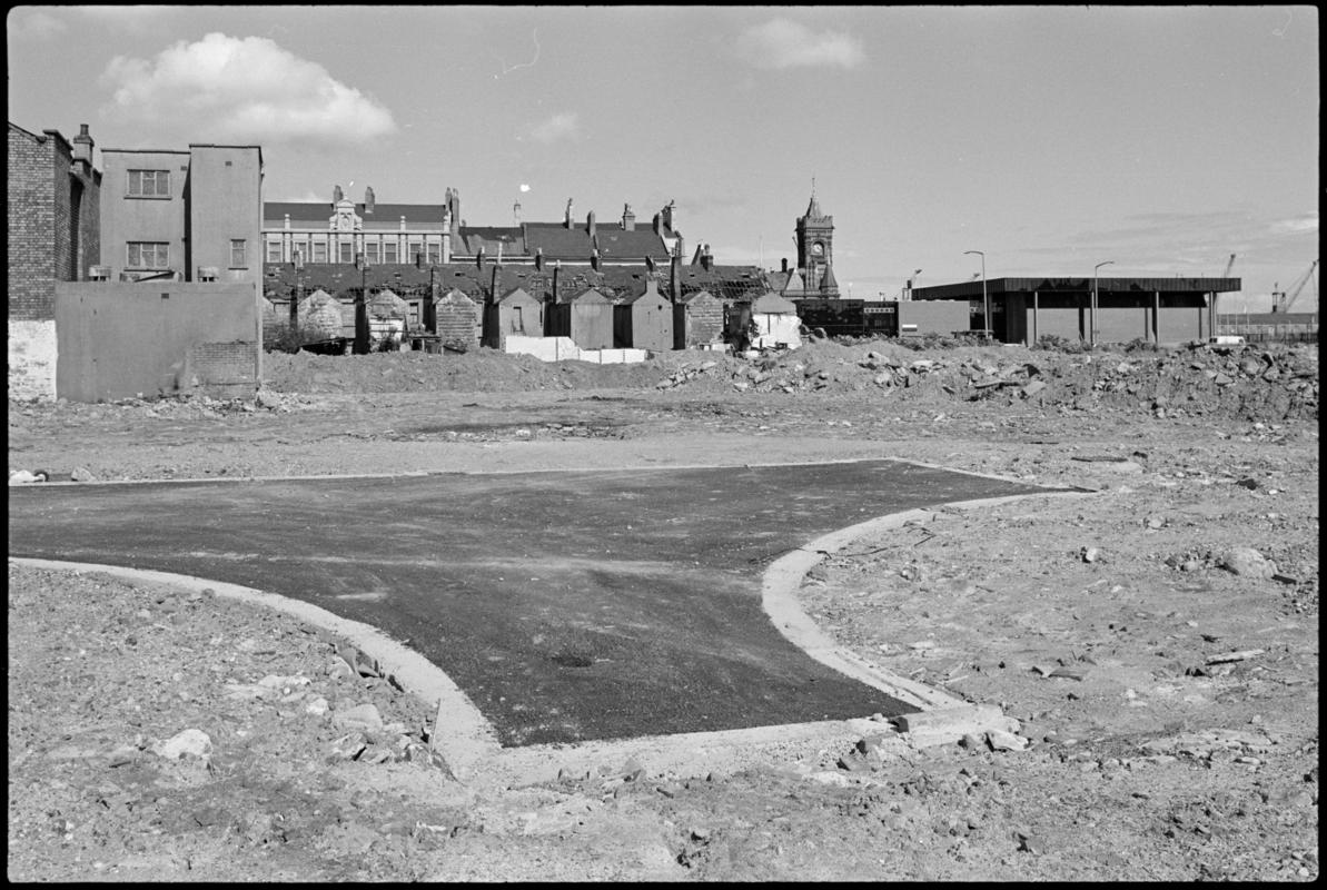 New tarmac on cleared ground near Stuart Street, Butetown, with disused houses and tower of the Pierhead building in the background.