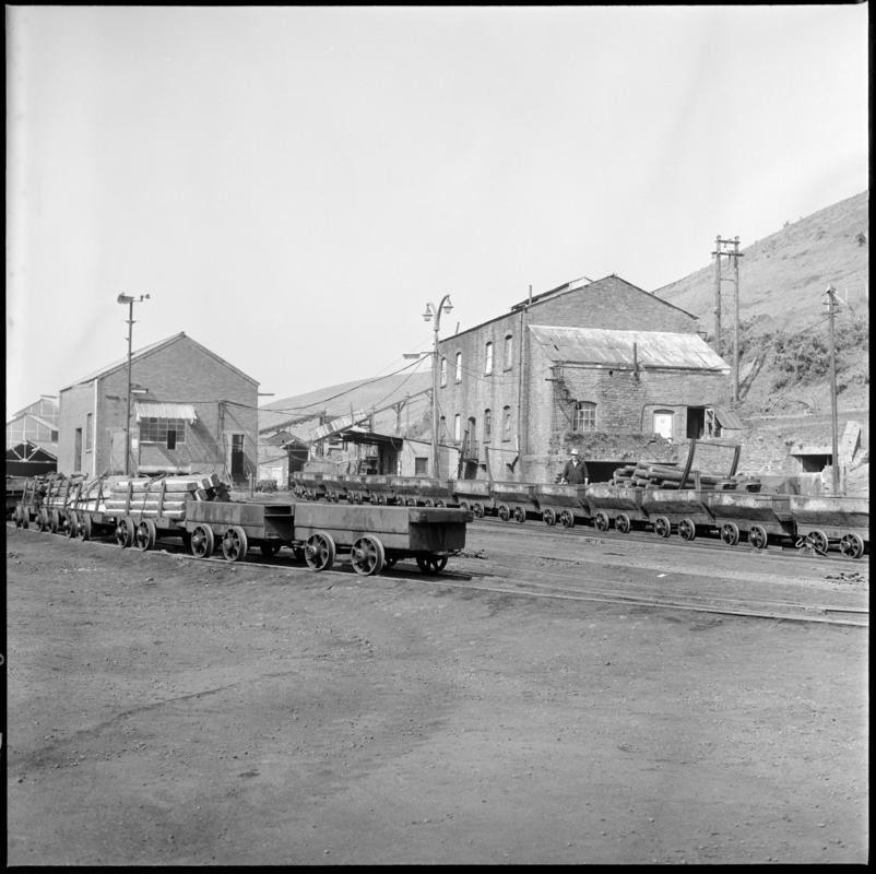Black and white film negative showing Graig Merthyr Colliery yard in 1977 with a long journey of drams waiting to be run into the mine.  In the foreground are special cut-down drams used for moving supplies.  &#039;Graig Merthyr&#039; is transcribed from original negative bag.