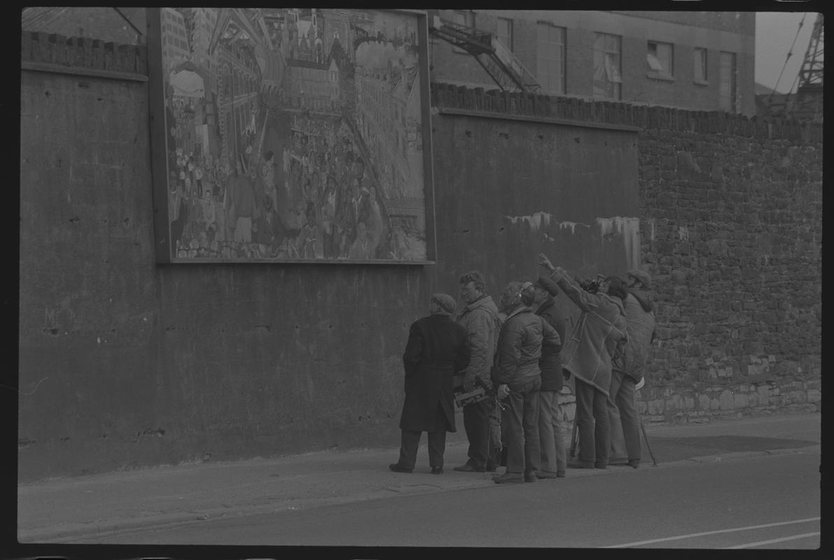 Group looking at mural on wall of railway embankment.