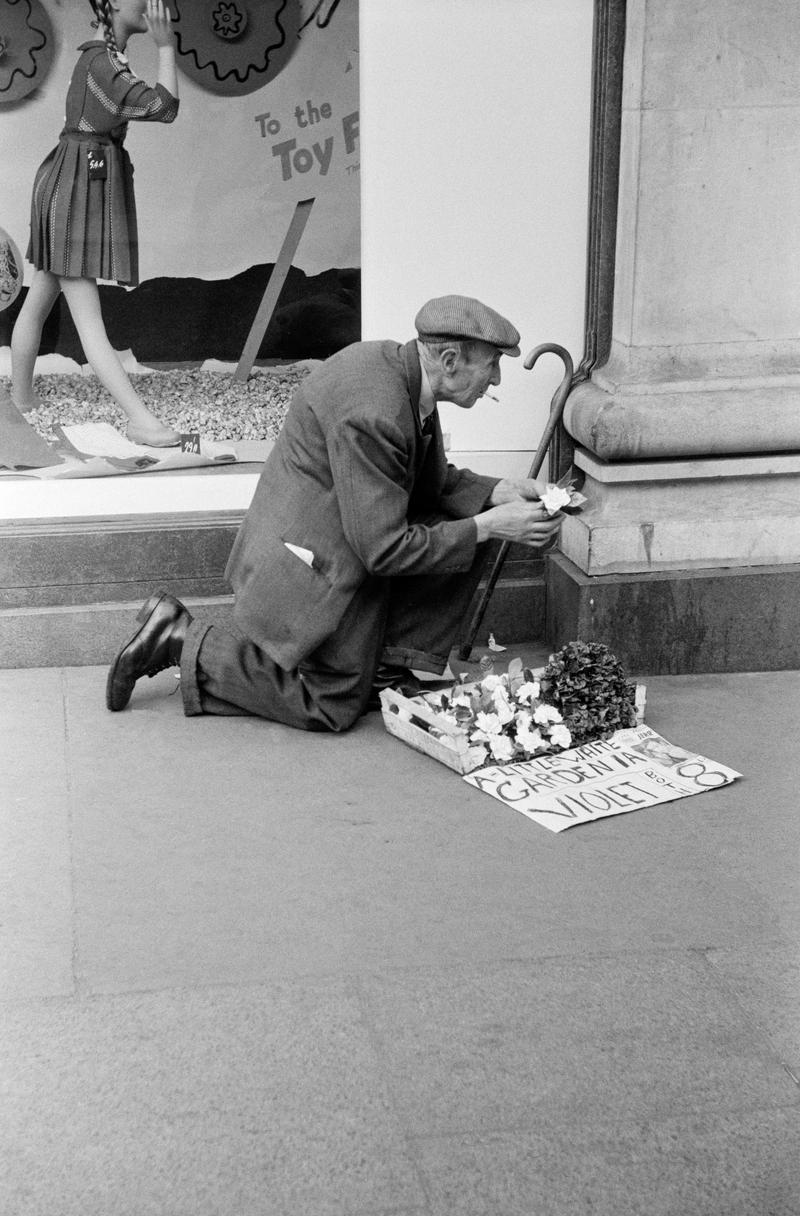 GB. ENGLAND. London. Street trader in Oxford Street. One of the first pictures ever taken by David Hurn, shot on a Kodak folding Retina camera (first camera). 1955.