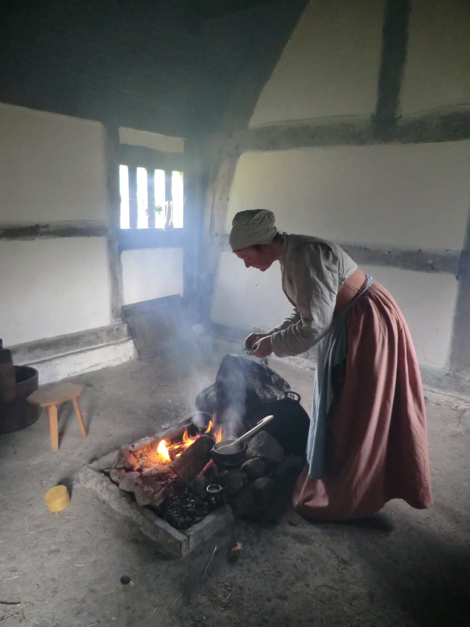 A woman dressed in 1530s style adds spices to a cauldron
