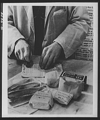 A shopkeeper cancels the coupons in a British housewife's ration book for the tea, sugar, cooking fats and bacon she is allowed for one week. Most foods in Britain are rationed and some brand names are given the designation 