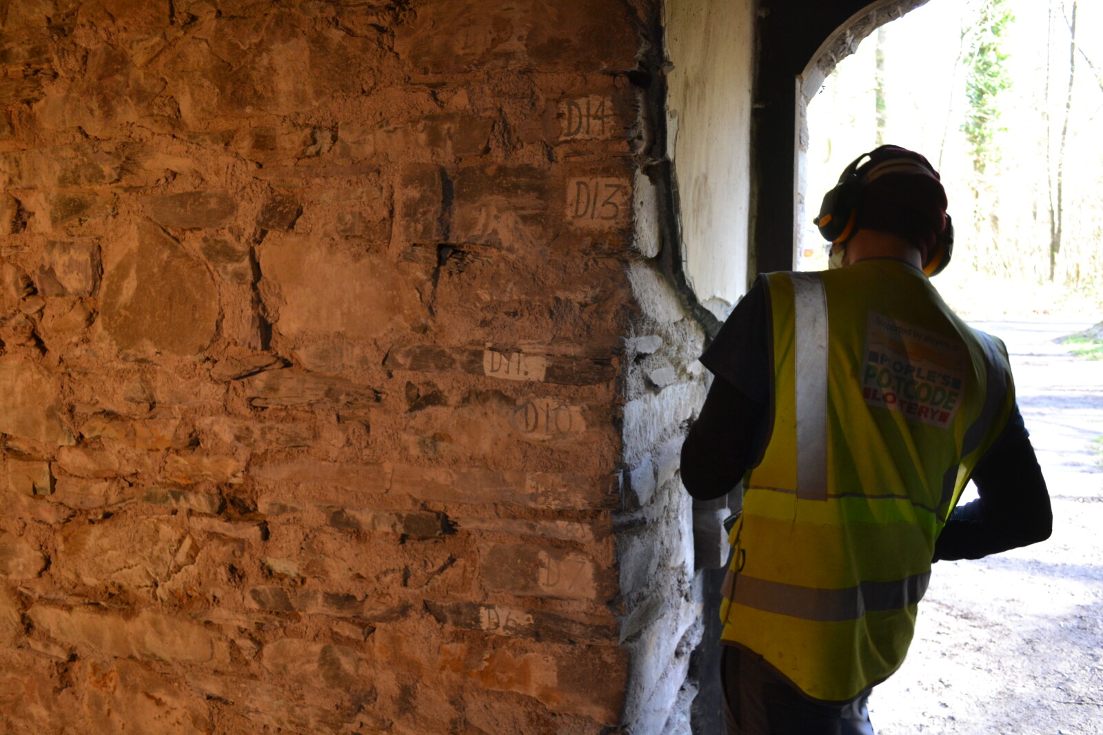 Workman next to a newly stripped stone wall revealing numbered cornerstones.