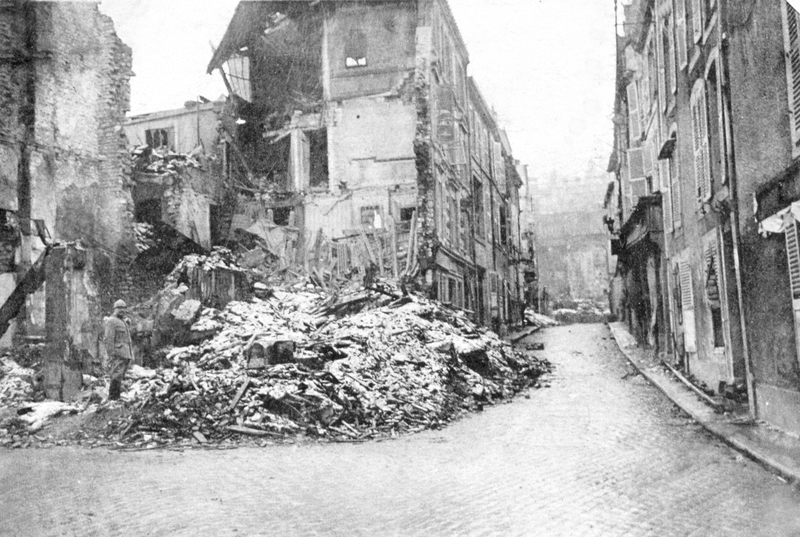 Black-and-white photograph of a road junction in a French city, with the building on one corner reduced to rubble