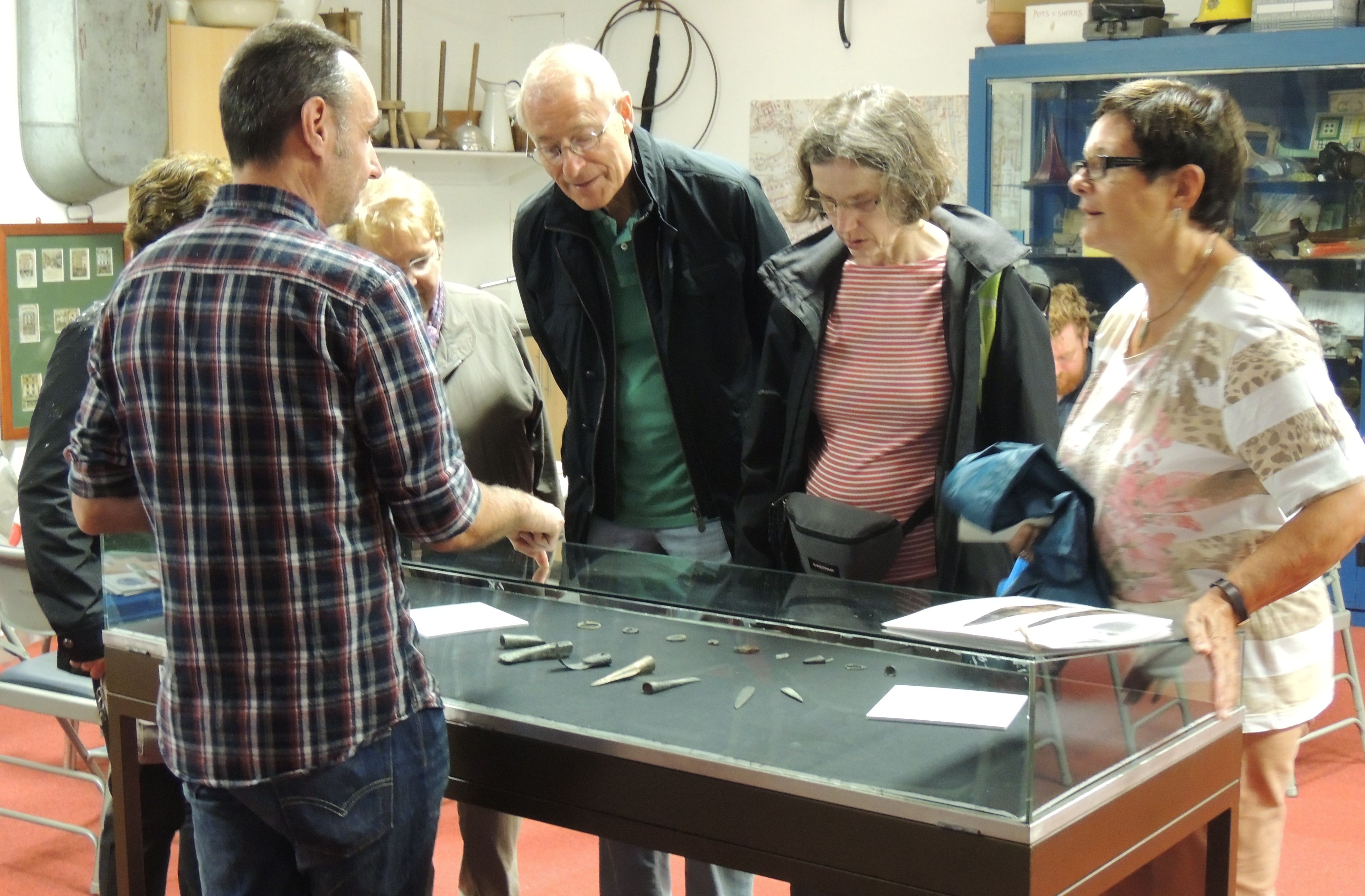 People are gathered around a small display case of objects acquired for Swansea Museum. 