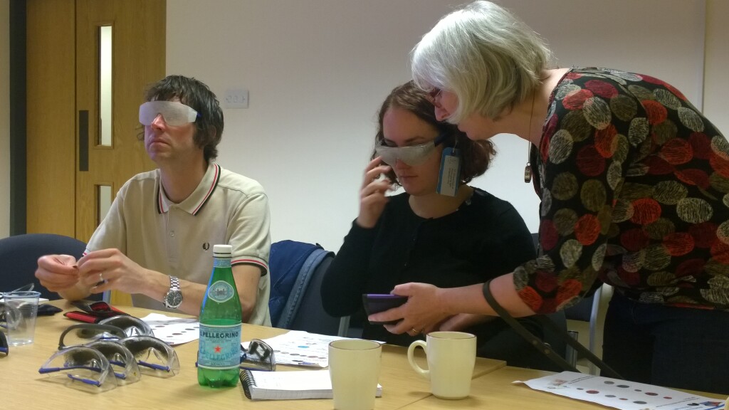 Two members of Museum staff wearing simulation spectacles counting out coins from a purse, overseen by the course trainer Sian