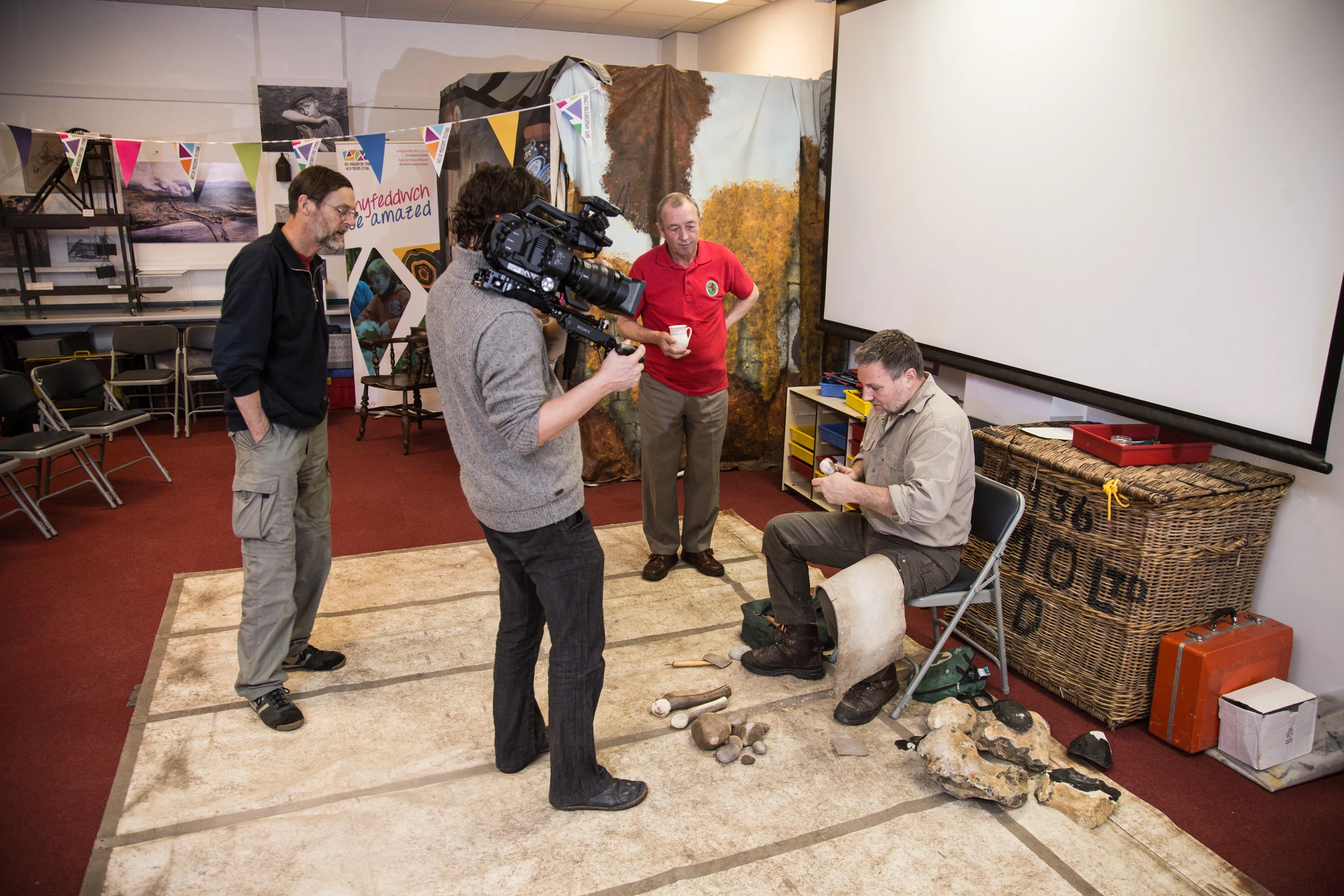 A cameraman is filming the flint knapper at work.