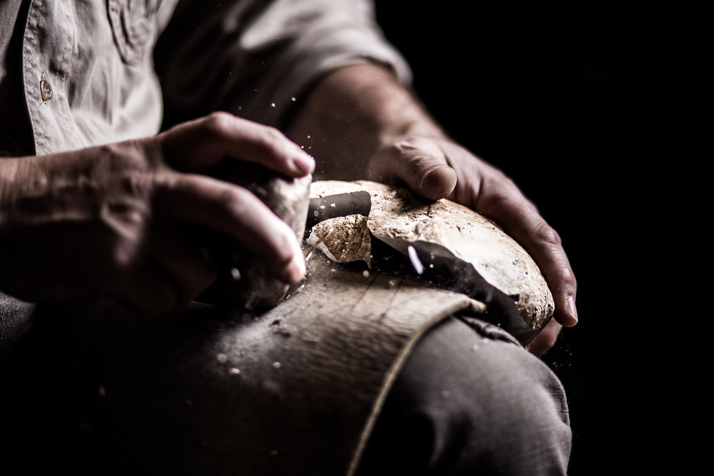 Close up of a man shaping a piece of flint with an antler