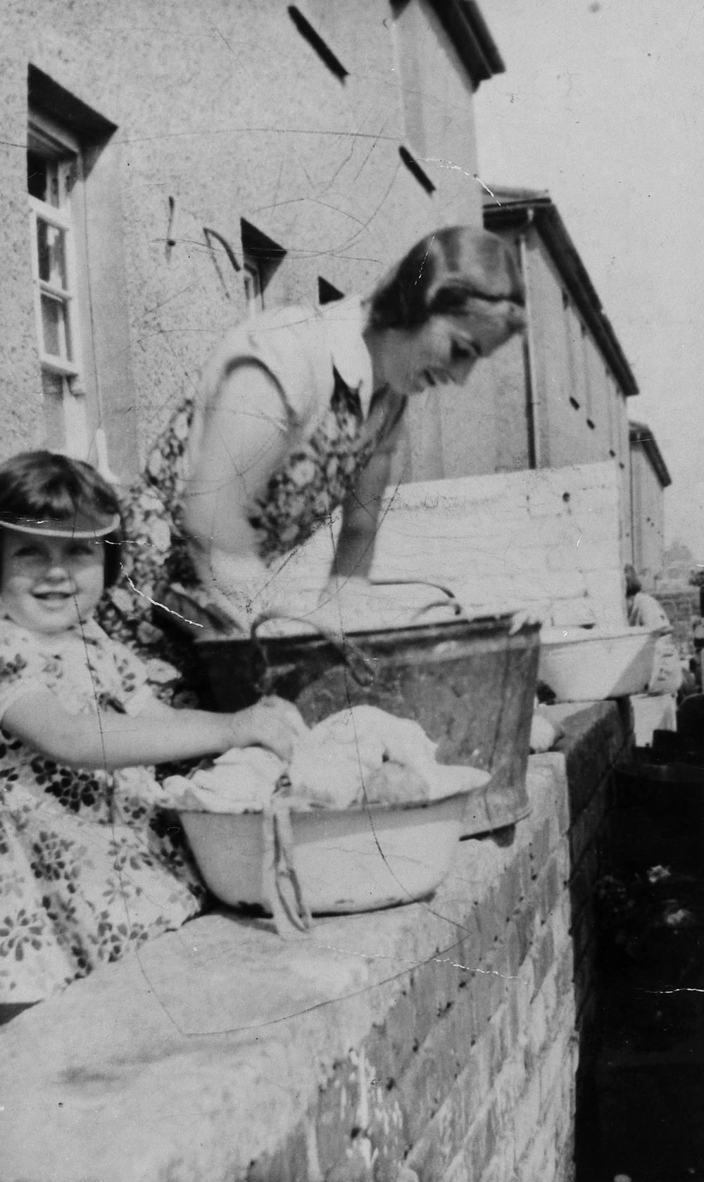Image of woman and child washing clothes in a zinc bath on the garden wall at Pyle, Mid Glamorgan, 1930s.
