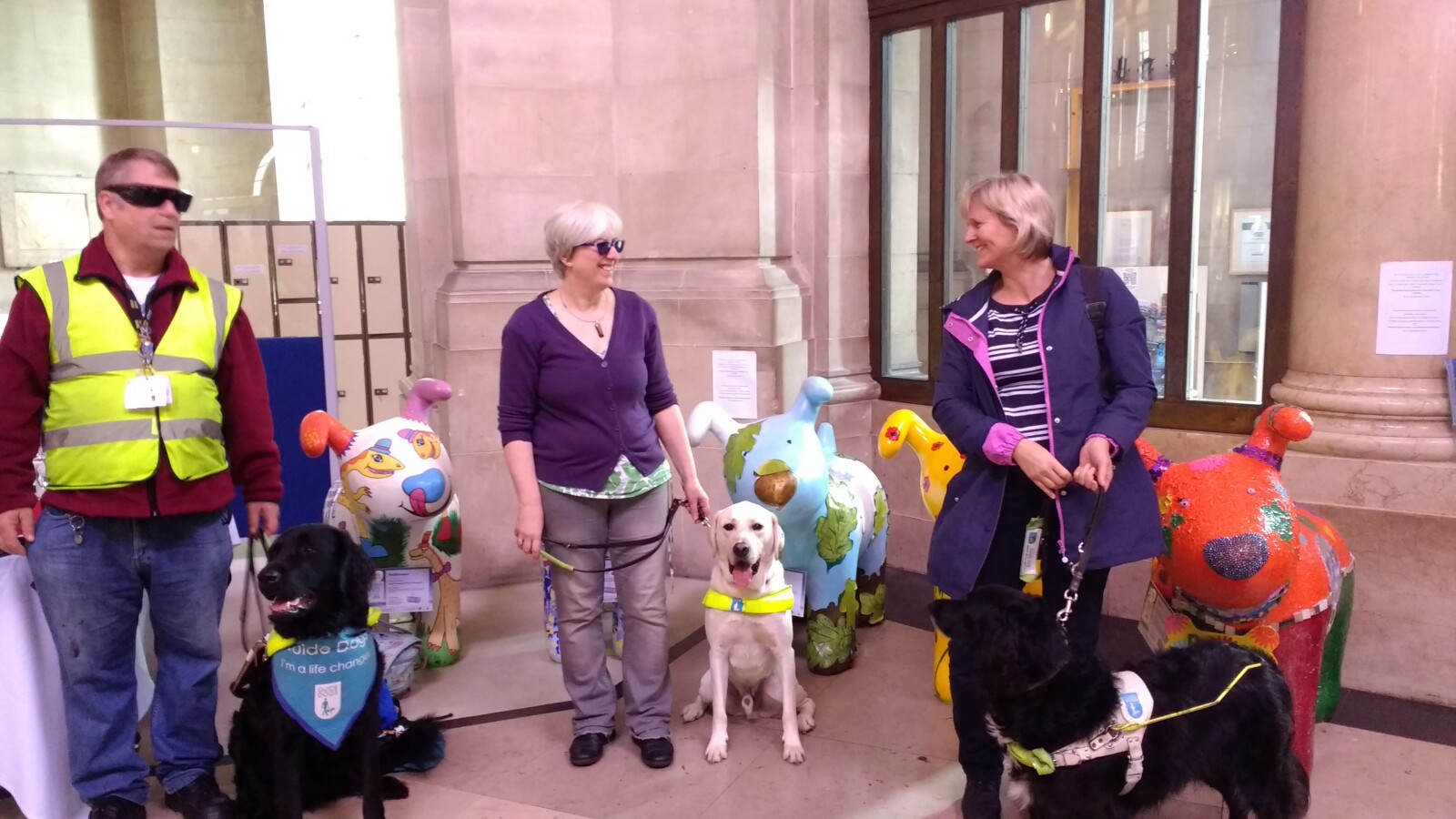 Three Guide Dogs and their owners standing next to the Snowpup sculptures at National Museum Cardiff