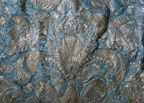 Section of blue damask fabric with intricate silver thread embroidery.