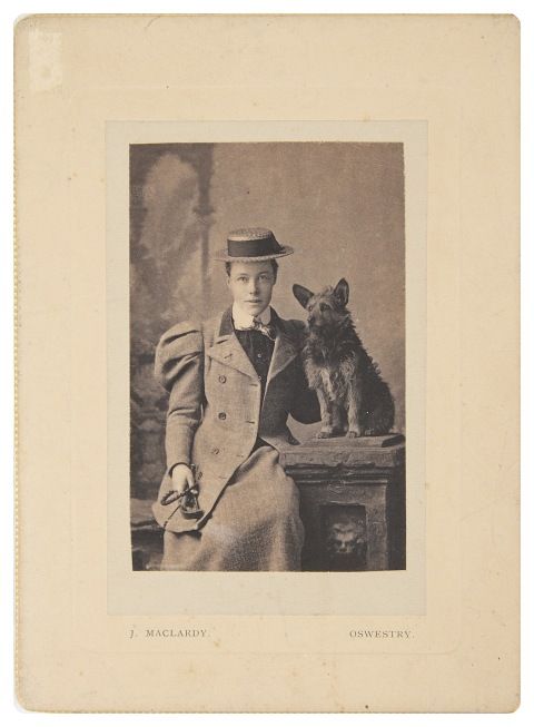 black and white photo of a woman wearing a jacket, standing next to a dog