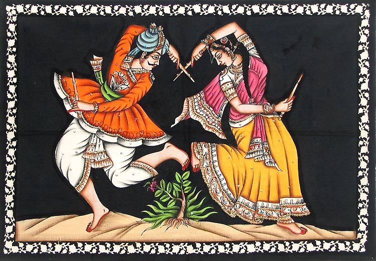 A barefoot man and woman in brightly coloured clothing performing a Hindu circle stick dance.  Between the two dancers there is a small plant with a pink flower growing through the sand.