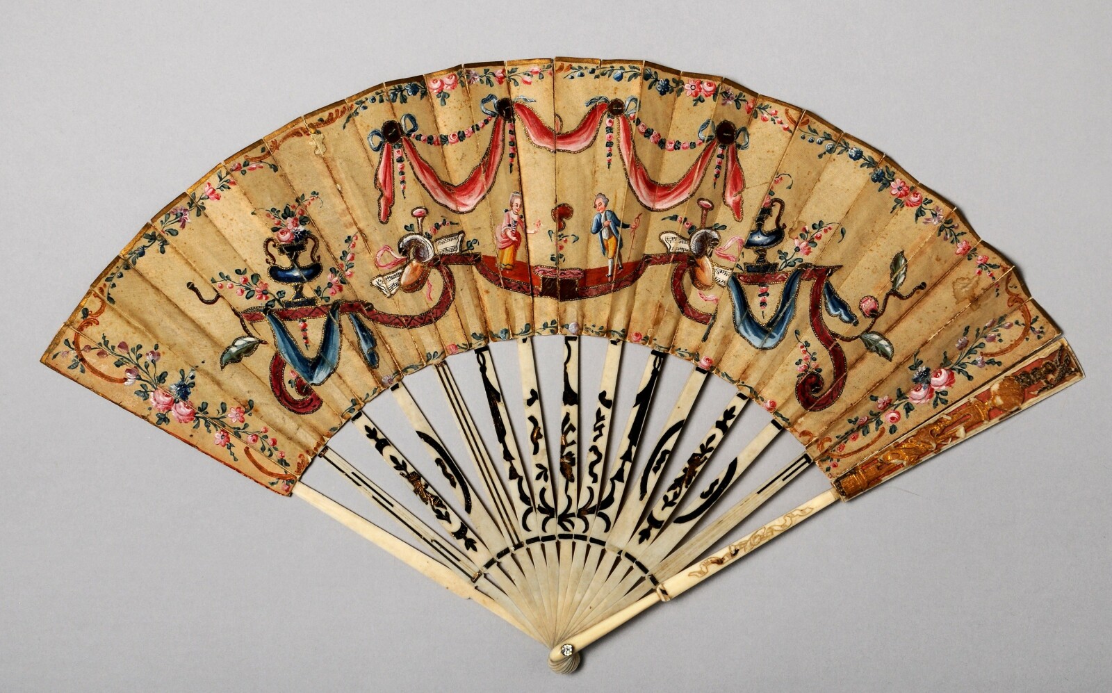 Fan with colourful painted images of men and women, flowers, swags and sequins.