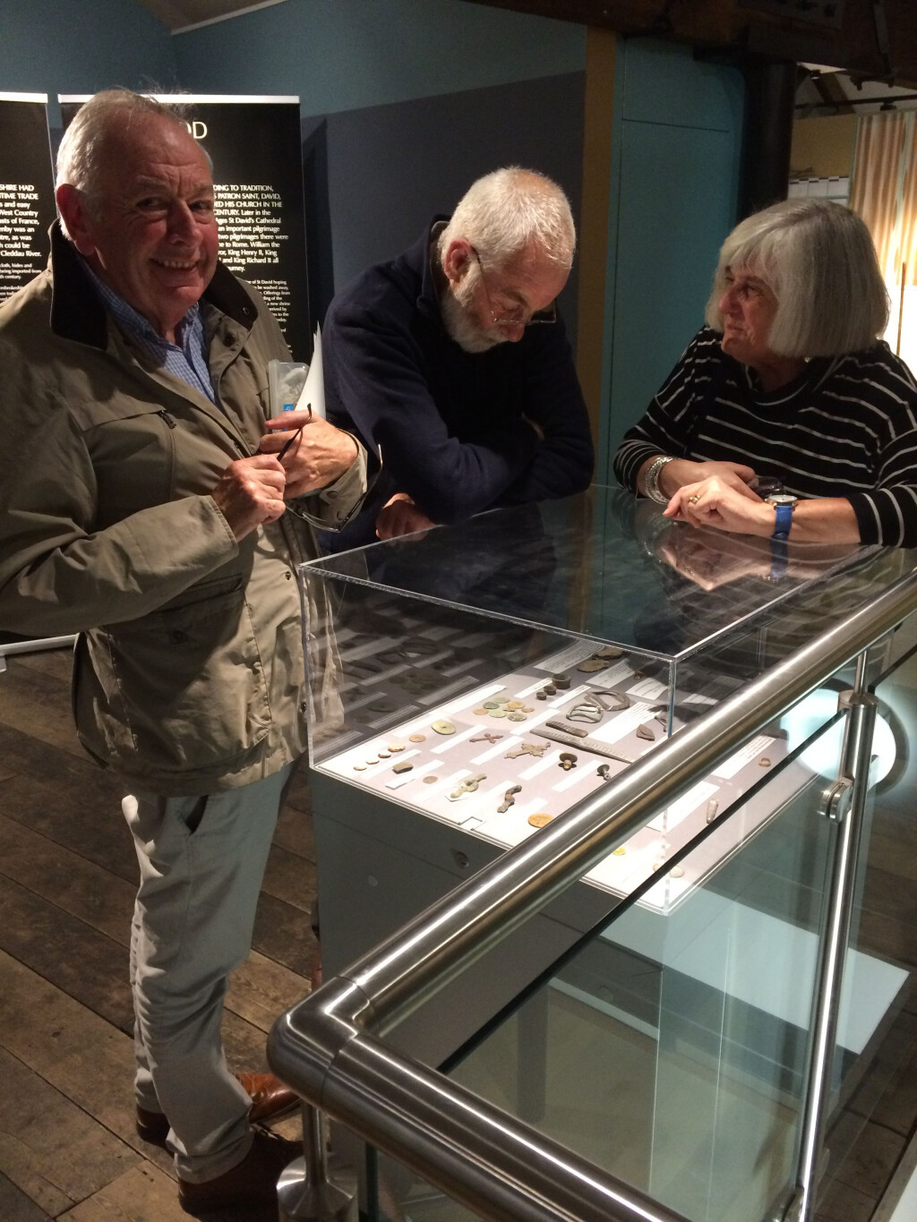 Three people are looking at objects in a display case.