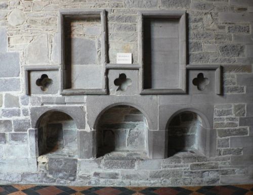 A picture of a stone wall in a cathedral with openings of vrious shapes and sizes.