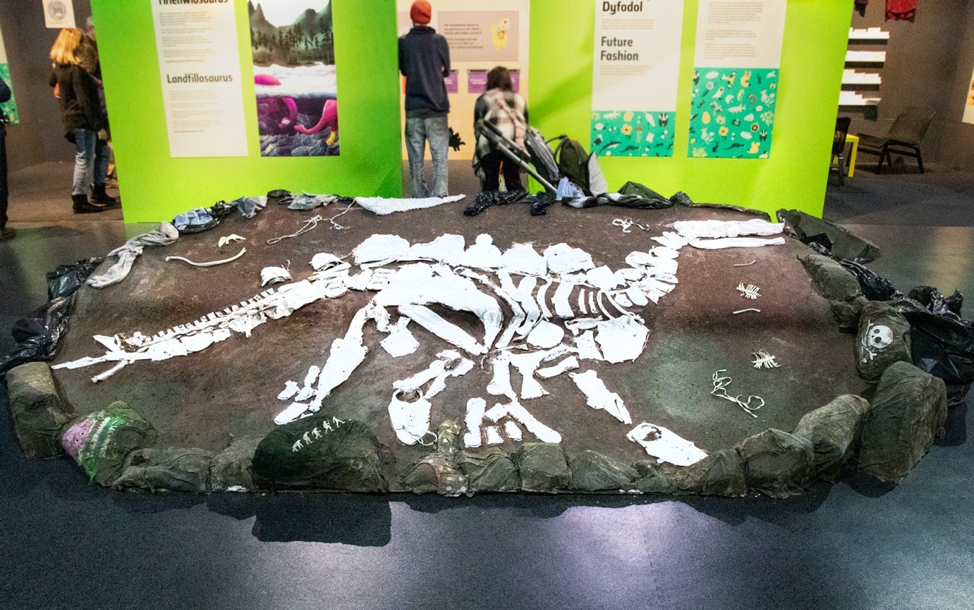 A photo of a display i the Dippy About nature exhibition. It shows a a model skeleton of a stegosaurus made from pieces of white clothing stuck to a large brown board.