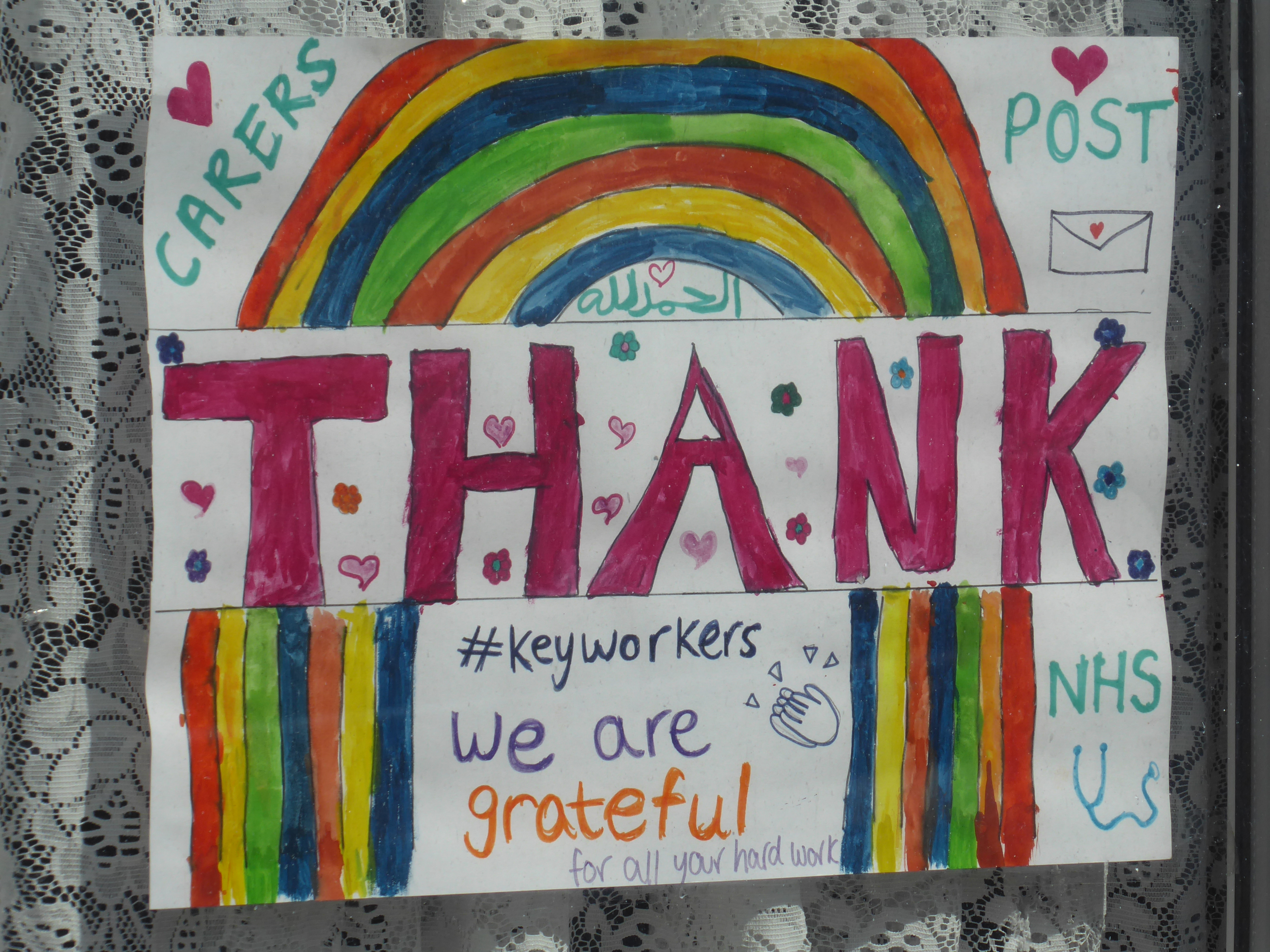 Hand-drawn rainbow on a piece of white paper on display in a house window. The sign is inscribed: 'THANK YOU KEY WORKERS We are grateful for all your hard work'.