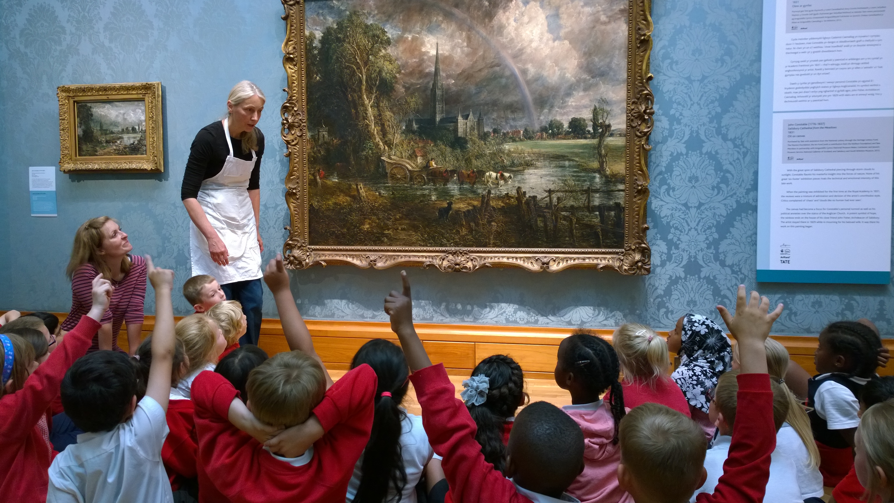 A group of school children sitting in an art gallery discussing Constable's painting with an artist