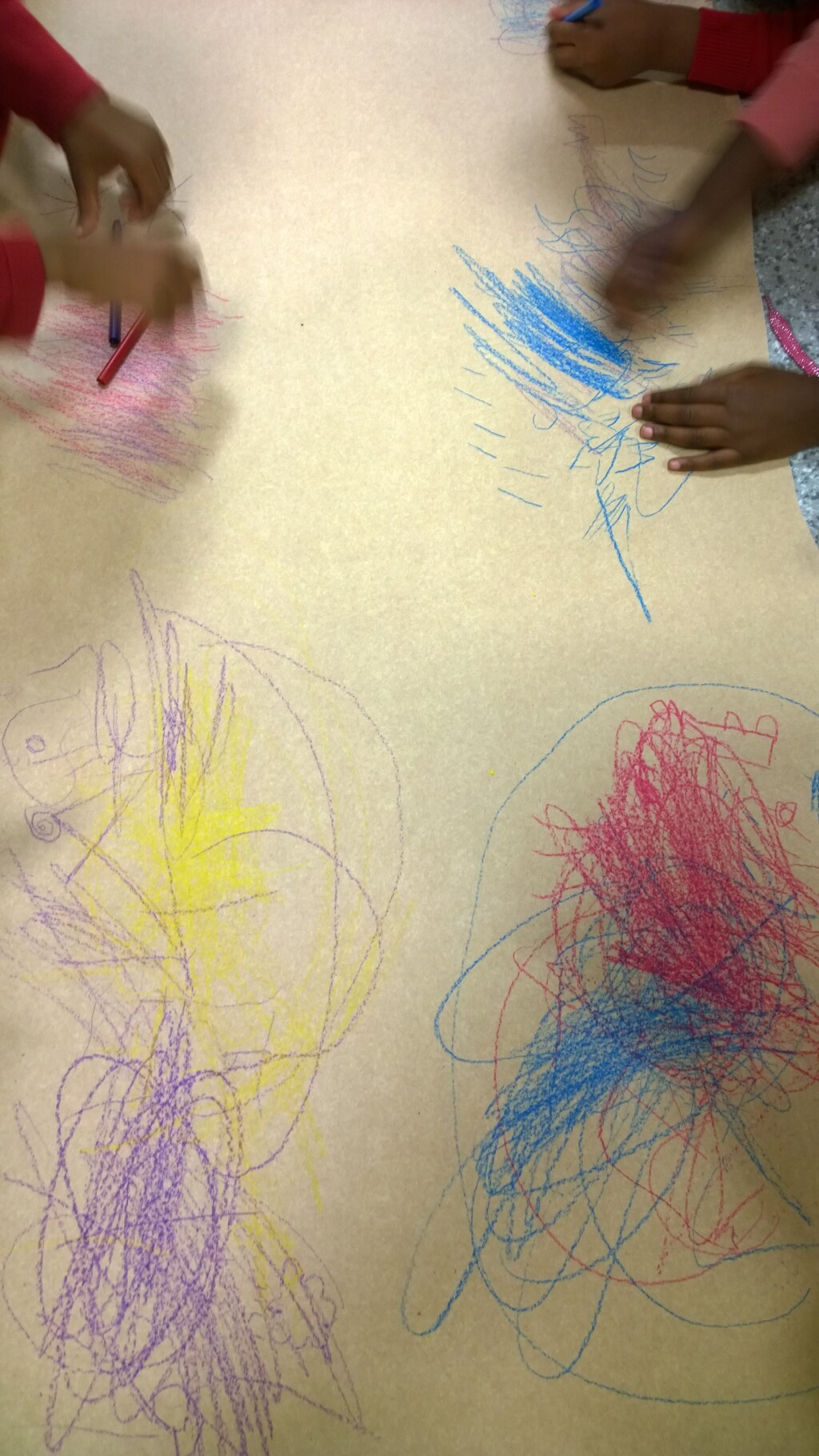 Children creating different marks with coloured pencils on a large sheet of paper