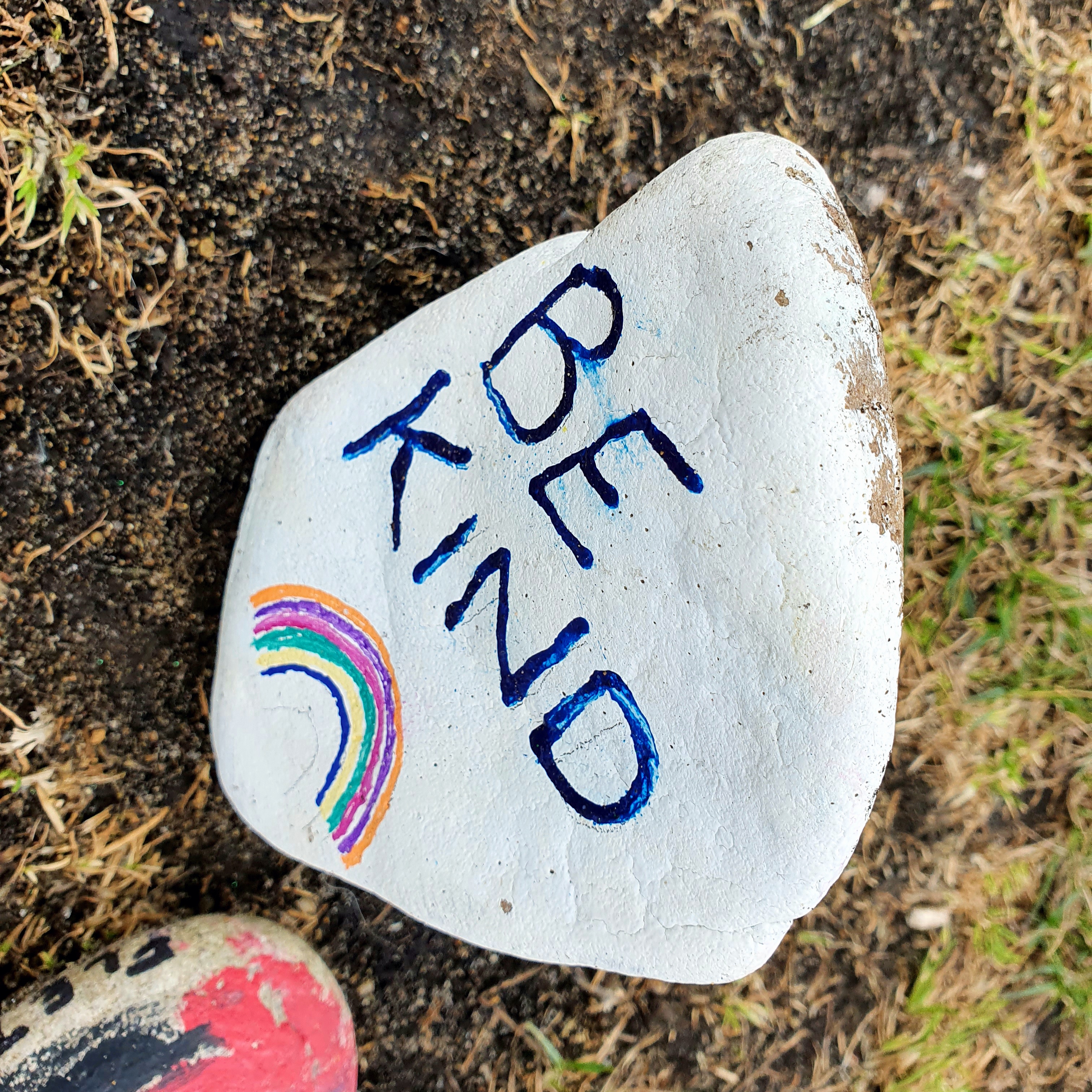 A small stone hand-painted with the words BE KIND and a rainbow