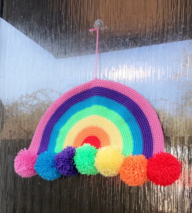 Colourful crocheted rainbow with pompoms displayed on a front door. 