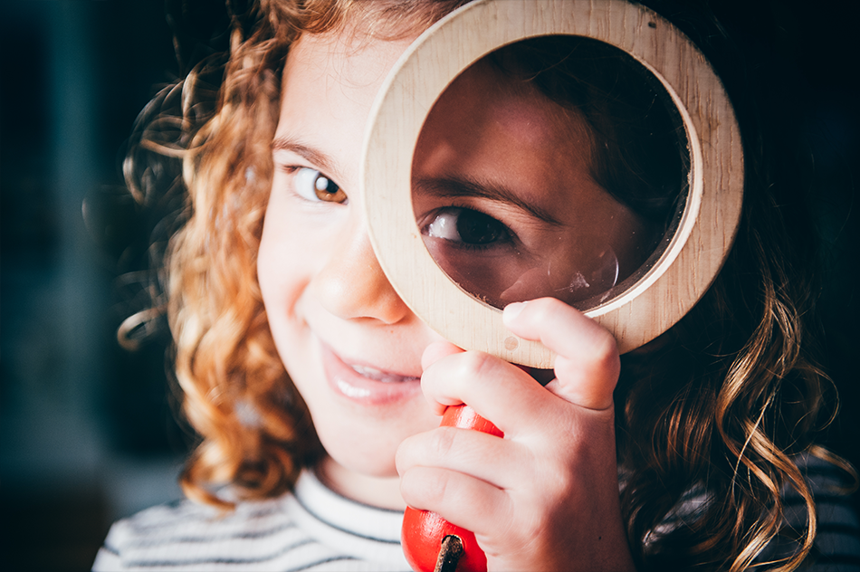 Young girl looking through a wooden magnifying glass