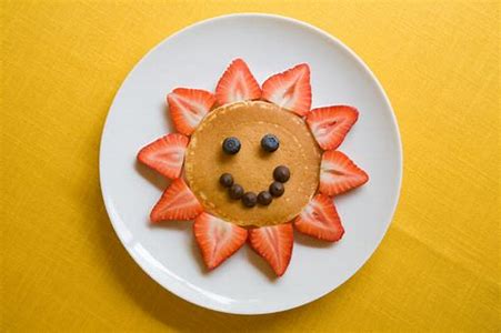 A picture of a smiley face made of a pancake, blueberries and sliced strawberries