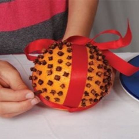 Photo of a pomander, an orange studded with cloves and wrapped in a red ribbon