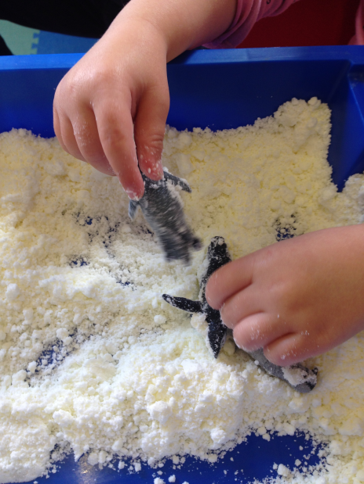 Photo of a child playig with toy penguins in fake snow