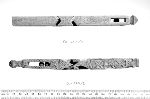 Black-and-white photograph of two long, thin, wooden artefacts with patterns carved onto them, placed above a ruler which shows them to be a little over 20cm long.