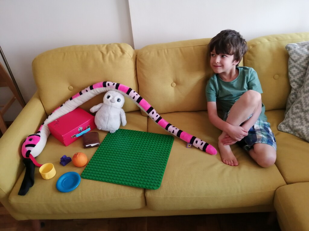 Photo of a child sitting on a sofa next to a collection of toys of different colours