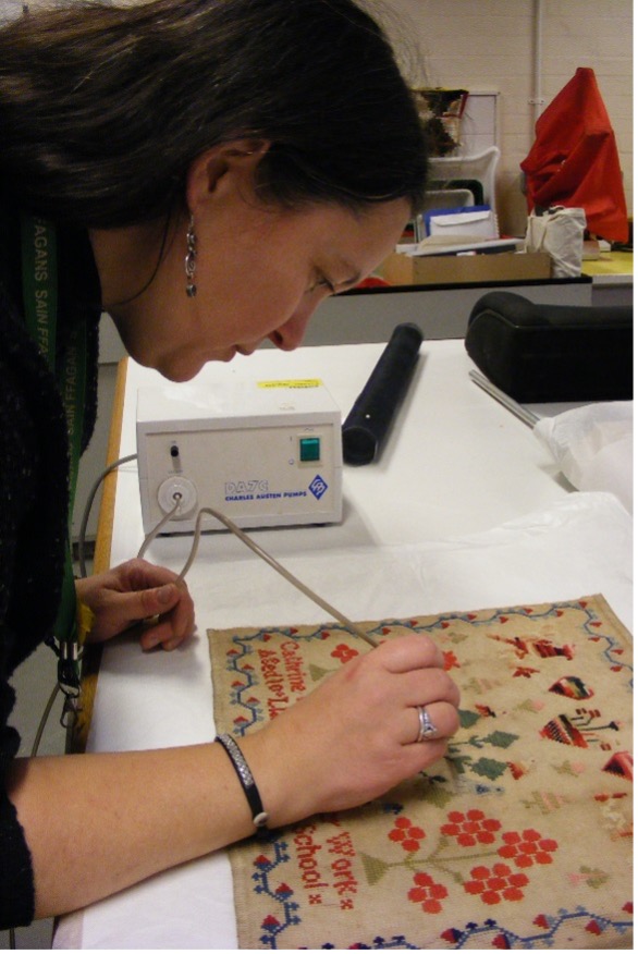 A woman working on an antique textile.