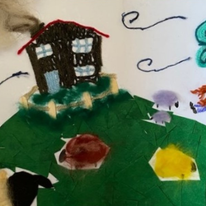 Picture of a house on a hill with a tree and sheep, made from scrapes of wool and felt