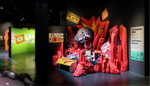Photo of a museum exhibition showing a meteor crashing into dinosaurs made from recycled materials