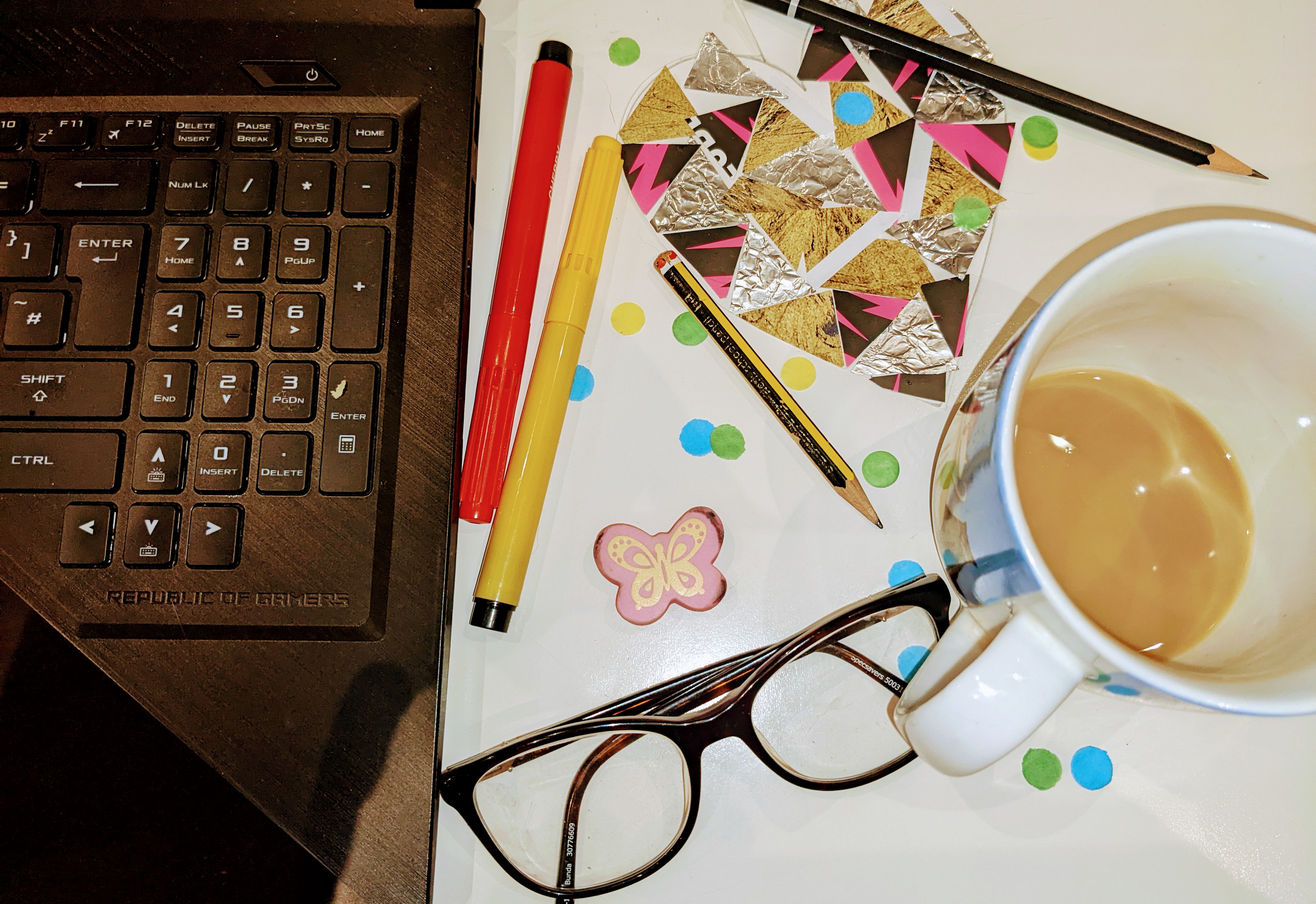 photograph of computer keyboard, glasses, cup and coloured paper