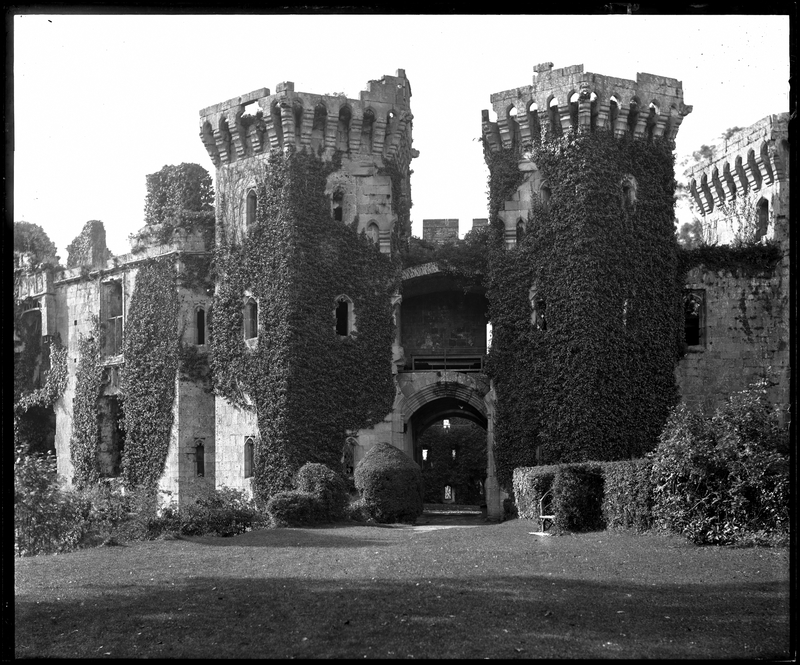 Black-and-white photograph of a castle gatehouse, largely covered with ivy
