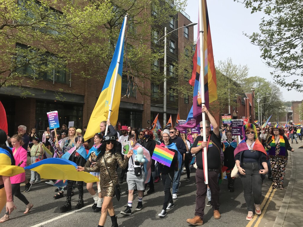 Picture of the Pride Swansea parade with individuals holding LGBTQ+ banner and a Ukrainian banner