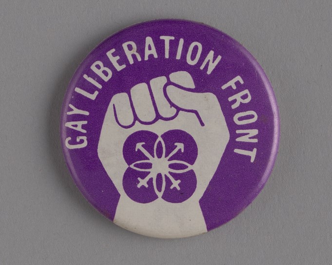 A purple badge with a white fist in the centre. The words Gay Liberation Front around the edge in white text 