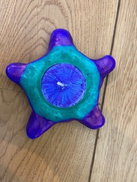 Photograph of a star shaped blue candle holder with a turquoise circle at the centre of the star and a blue candle 