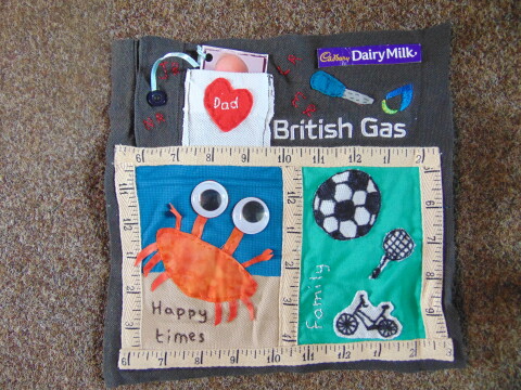 Photograph of a patchwork square which has a grey background, with a crab next to the words happy times a white pocket, the name British Gas, a football, tennis racquet and bike