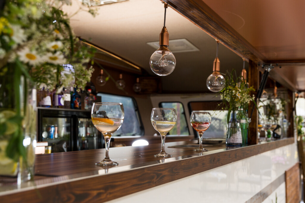 A bar counter with three large glasses of gin, decorated with stylish lights and fresh flowers