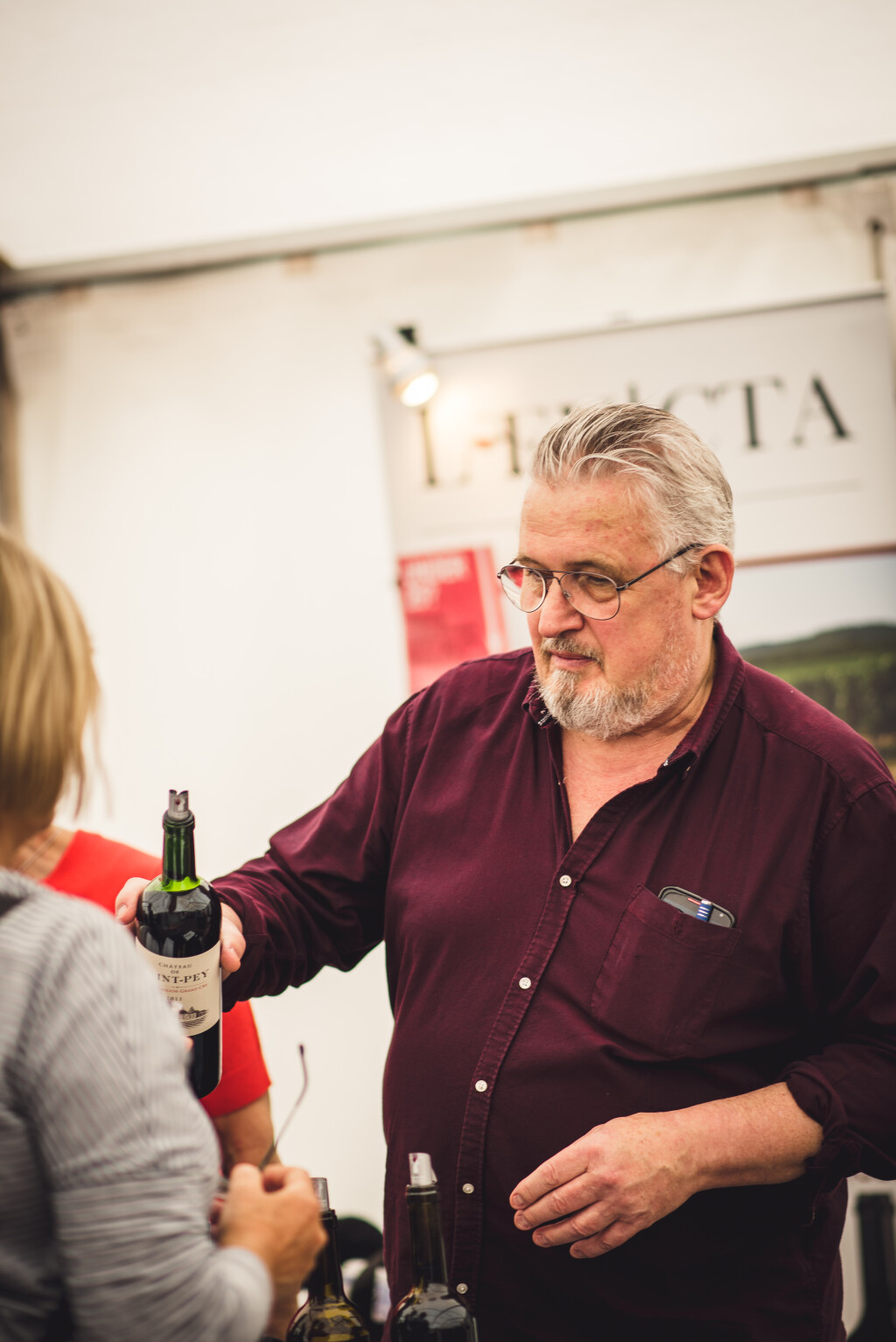 A trader holding a bottle of wine serving some tasters to a customer