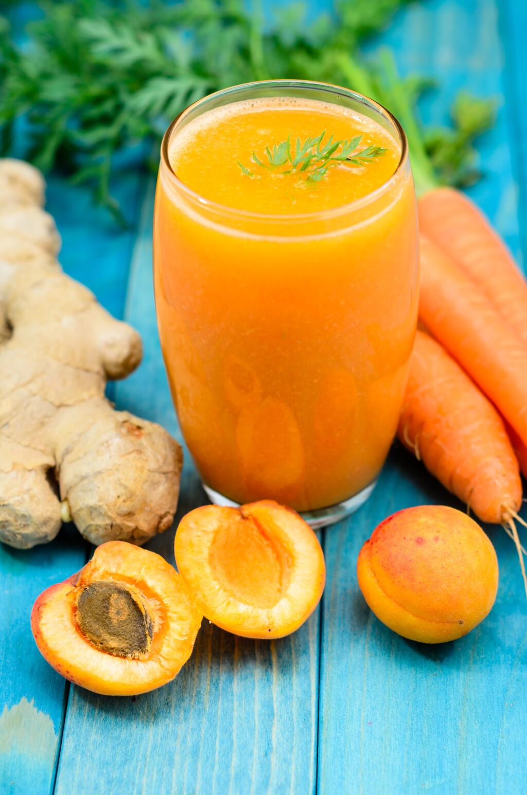 A cup of orange juice with carrots, ginger and peaches surrounding the cup